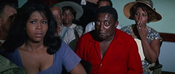 Movie still from “The Learning Tree” (1969), directed by Gordon Parks – A man in a red shirt is looking at a woman in a blue dress; Medium shot, High angle