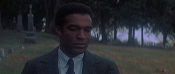 Movie still from “The Learning Tree” (1969), directed by Gordon Parks – A man wearing a suit and tie standing in a field; Close Up shot, Low angle