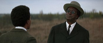 Movie still from “The Learning Tree” (1969), directed by Gordon Parks – A man in a suit and a hat standing next to another man in a suit; Close Up shot, Over the shoulder angle