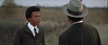 Movie still from “The Learning Tree” (1969), directed by Gordon Parks – A man in a suit and hat talking to another man in a suit and hat; Close Up shot, Over the shoulder angle