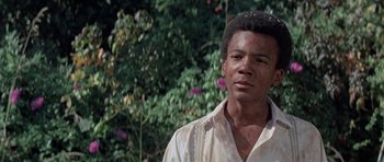 Movie still from “The Learning Tree” (1969), directed by Gordon Parks – A man in a white shirt is standing in front of some bushes; Close Up shot, Low angle