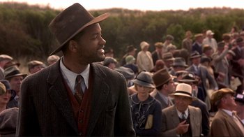 Movie still from “The Legend of Bagger Vance” (2000), directed by Robert Redford – A man in a suit and hat standing in front of a group of people; Medium shot, Over the shoulder angle