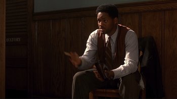 Movie still from “The Legend of Bagger Vance” (2000), directed by Robert Redford – A man sitting on a chair holding a pair of shoes in his hand; Medium shot, High angle