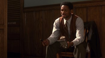 Movie still from “The Legend of Bagger Vance” (2000), directed by Robert Redford – A man sitting on a chair holding a phone; Medium shot, Low angle