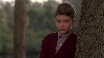 Movie still from “The Legend of Bagger Vance” (2000), directed by Robert Redford – A young boy in a red sweater leaning against a tree; Close Up shot, Over the shoulder angle