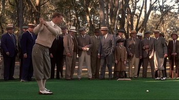 Movie still from “The Legend of Bagger Vance” (2000), directed by Robert Redford – A group of men in suits and hats standing on a grass field; Wide shot, Low angle