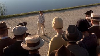 Movie still from “The Legend of Bagger Vance” (2000), directed by Robert Redford – A group of people are gathered around a man holding a stick; Wide shot, High angle