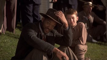 Movie still from “The Legend of Bagger Vance” (2000), directed by Robert Redford – A man in a suit and a hat sitting next to another man; Medium shot, Over the shoulder angle