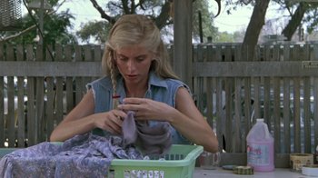 Movie still from “The Legend of Billie Jean” (1985), directed by Matthew Robbins – A woman sitting on the ground knitting a scarf; Medium shot, Low angle