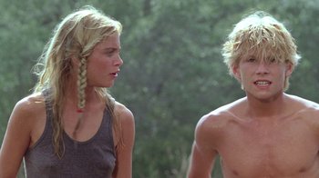 Movie still from “The Legend of Billie Jean” (1985), directed by Matthew Robbins – A man and a woman standing next to each other in front of trees; Medium shot, Low angle