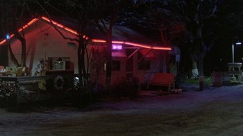 Movie still from “The Legend of Billie Jean” (1985), directed by Matthew Robbins – A man standing on a bench in front of a building at night; Extreme Wide shot, Low angle