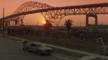 Movie still from “The Legend of Billie Jean” (1985), directed by Matthew Robbins – A car parked on the side of the road under a bridge; Extreme Wide shot, Over the shoulder angle