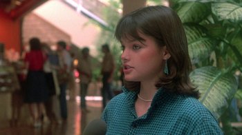 Movie still from “The Legend of Billie Jean” (1985), directed by Matthew Robbins – A young girl talking into a microphone in an indoor setting; Close Up shot, Over the shoulder angle