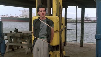 Movie still from “The Legend of Billie Jean” (1985), directed by Matthew Robbins – A man standing in front of a yellow container; Medium shot, Low angle