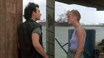 Movie still from “The Legend of Billie Jean” (1985), directed by Matthew Robbins – A man and a woman standing next to each other near a body of water; Medium shot, Over the shoulder angle
