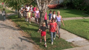 Movie still from “The Legend of Billie Jean” (1985), directed by Matthew Robbins – A group of people walking down a sidewalk near a tree; Wide shot, High angle