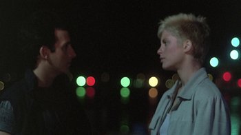 Movie still from “The Legend of Billie Jean” (1985), directed by Matthew Robbins – A man and a woman standing next to each other in front of lights; Close Up shot, Low angle