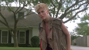 Movie still from “The Legend of Billie Jean” (1985), directed by Matthew Robbins – A woman in a brown jacket standing in front of a house; Medium shot, Low angle