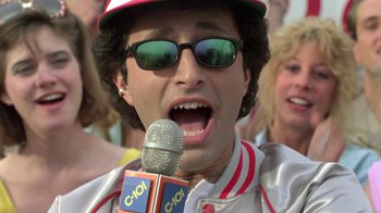 Movie still from “The Legend of Billie Jean” (1985), directed by Matthew Robbins – A man in a baseball uniform is holding a microphone; Close Up shot, Low angle