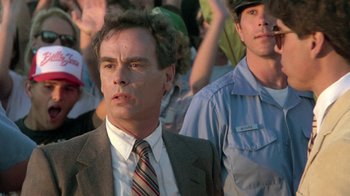 Movie still from “The Legend of Billie Jean” (1985), directed by Matthew Robbins – A man in a suit and tie in front of a group of people; Close Up shot, Over the shoulder angle