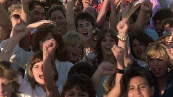 Movie still from “The Legend of Billie Jean” (1985), directed by Matthew Robbins – A group of people standing next to each other with their hands in the air; Medium shot, High angle