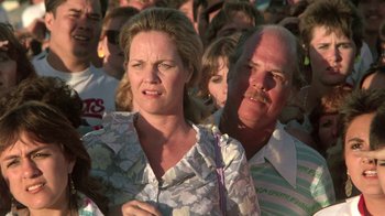 Movie still from “The Legend of Billie Jean” (1985), directed by Matthew Robbins – A woman and a man standing next to each other in front of a crowd; Close Up shot, High angle