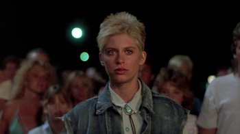 Movie still from “The Legend of Billie Jean” (1985), directed by Matthew Robbins – A woman with blonde hair is standing in front of a group of people; Close Up shot, Low angle