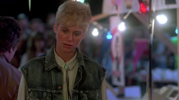 Movie still from “The Legend of Billie Jean” (1985), directed by Matthew Robbins – A woman with short blonde hair wearing a white shirt and a jean vest; Close Up shot, Over the shoulder angle