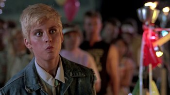 Movie still from “The Legend of Billie Jean” (1985), directed by Matthew Robbins – A young man standing in front of a group of people; Close Up shot, Over the shoulder angle
