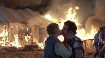 Movie still from “The Legend of Billie Jean” (1985), directed by Matthew Robbins – A couple of people kissing in front of a burning house; Wide shot, Over the shoulder angle