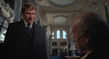 Movie still from “The Legend of Hell House” (1973), directed by John Hough – A man in a suit talking to another man in a suit; Medium shot, Low angle