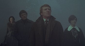 Movie still from “The Legend of Hell House” (1973), directed by John Hough – A man in a coat and tie standing next to another man in a suit; Medium shot, Low angle