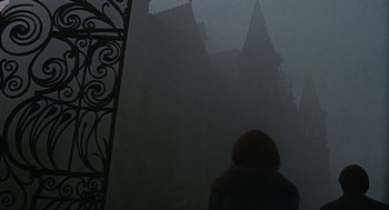 Movie still from “The Legend of Hell House” (1973), directed by John Hough – A person standing in front of a building in the fog; Wide shot, Low angle