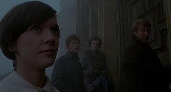 Movie still from “The Legend of Hell House” (1973), directed by John Hough – A woman standing next to a man and a woman; Close Up shot, Low angle
