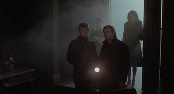 Movie still from “The Legend of Hell House” (1973), directed by John Hough – Two men are standing in a dimly - lit room; Medium shot, Low angle