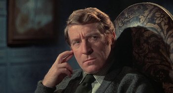 Movie still from “The Legend of Hell House” (1973), directed by John Hough – A person sitting in a chair with his hand to his ear; Close Up shot, Low angle