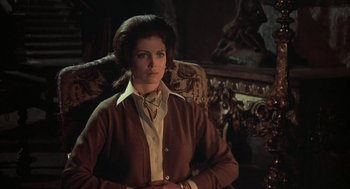 Movie still from “The Legend of Hell House” (1973), directed by John Hough – A woman standing in a chair wearing a brown jacket; Medium shot, Low angle