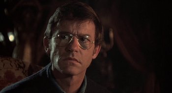 Movie still from “The Legend of Hell House” (1973), directed by John Hough – A person wearing glasses and a jacket; Close Up shot, Over the shoulder angle