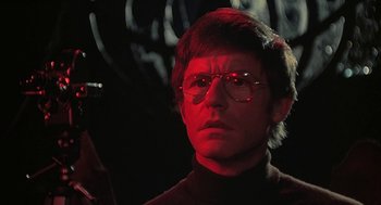 Movie still from “The Legend of Hell House” (1973), directed by John Hough – A man in a black shirt and red glasses; Close Up shot, Low angle