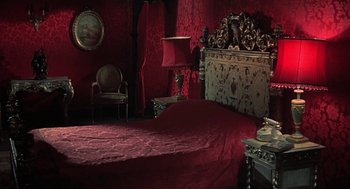 Movie still from “The Legend of Hell House” (1973), directed by John Hough – A bed room with a bed and a lamp in it; Wide shot, High angle