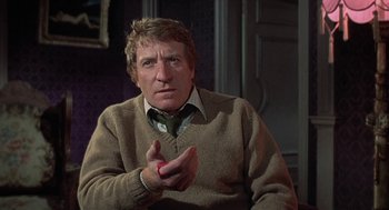 Movie still from “The Legend of Hell House” (1973), directed by John Hough – A man wearing a sweater claps his hands; Medium shot, Over the shoulder angle