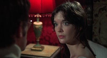 Movie still from “The Legend of Hell House” (1973), directed by John Hough – A young woman looking into the camera with a lamp in the background; Close Up shot, Over the shoulder angle