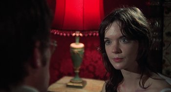 Movie still from “The Legend of Hell House” (1973), directed by John Hough – A woman sitting in front of a red lamp on a night stand; Close Up shot, Over the shoulder angle