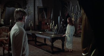 Movie still from “The Legend of Hell House” (1973), directed by John Hough – A woman standing in front of a table with candles on it; Wide shot, Over the shoulder angle