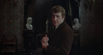 Movie still from “The Legend of Hell House” (1973), directed by John Hough – A man in a suit and tie clasping his hands; Medium shot, Over the shoulder angle
