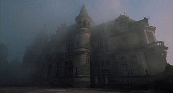 Movie still from “The Legend of Hell House” (1973), directed by John Hough – A very tall building in the middle of a foggy day; Extreme Wide shot, Low angle