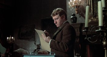 Movie still from “The Legend of Hell House” (1973), directed by John Hough – A man writing on a piece of paper in a room; Close Up shot, Low angle