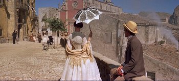 Movie still from “The Leopard” (1963), directed by Luchino Visconti – A woman holding an umbrella while standing next to a man; Wide shot, Low angle
