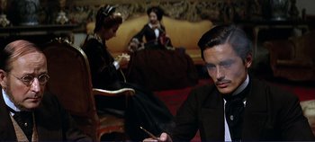 Movie still from “The Leopard” (1963), directed by Luchino Visconti – A man sitting in front of two women in a living room; Medium shot, Over the shoulder angle