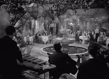 Movie still from “The Leopard Man” (1943), directed by Jacques Tourneur – A group of people sitting around a fountain in an outdoor restaurant; Wide shot, High angle